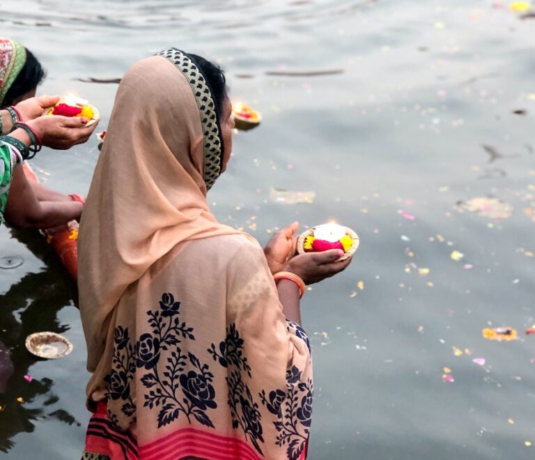 woman wearing pink hijab holding candle while standing on body of water